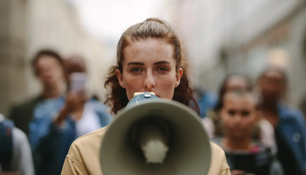 image shows a person speaking into a megaphone with a crowd in the background